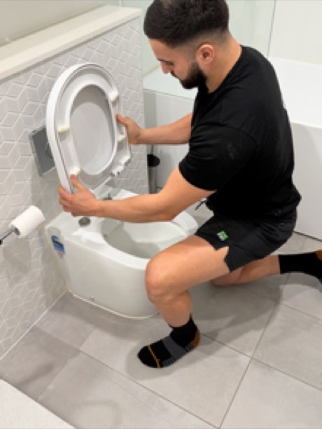 Plumber working on a wall-faced toilet in a tiled bathroom